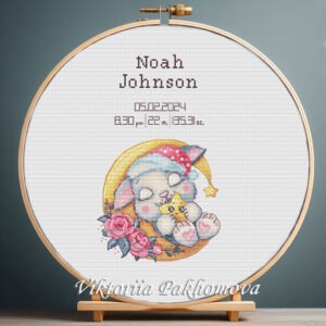 Cross stitch embroidery of a personalized sleeping bunny birth announcement displayed in a wooden hoop with custom newborn details.