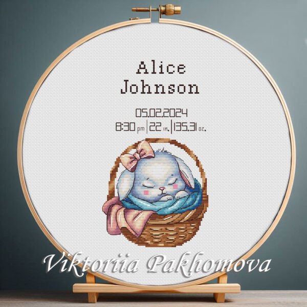 Cross stitch embroidery of a personalized baby girl birth announcement with a sleeping bunny displayed in a wooden hoop