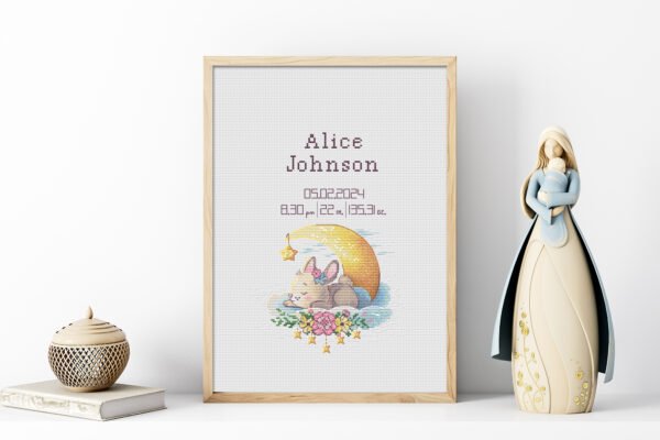 Framed sleeping bunny birth announcement cross stitch featuring personalized name, date and stats for baby girl nursery décor.