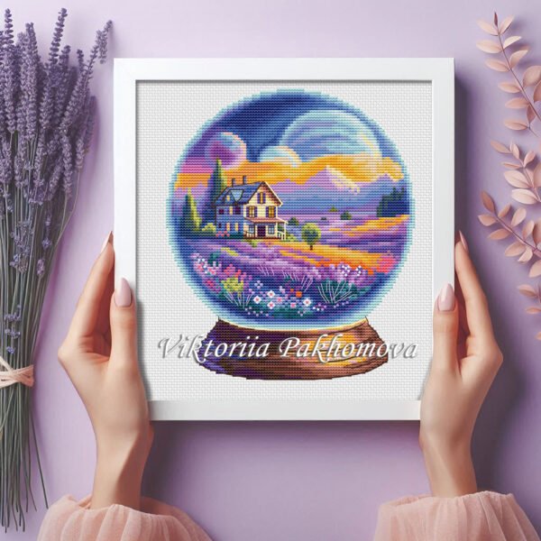33 Framed cross stitch artwork showing a glass ball with a lavender field, cozy house and bright sky.