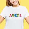 Rainbow dinosaur‑shaped alphabet letters from a cross stitch design stiched on a kids’ t‑shirt.