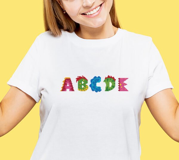 Rainbow dinosaur‑shaped alphabet letters from a cross stitch design stiched on a kids’ t‑shirt.