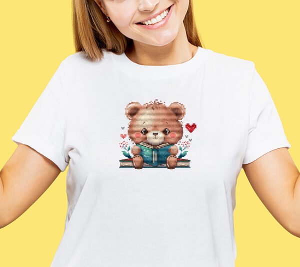 cross stitch of a woodland bear reading a book with cozy floral accents on t-shirt