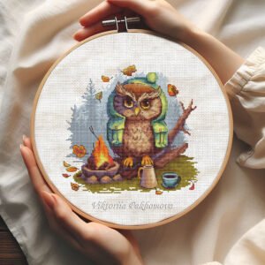 Cross stitch embroidery of a camping owl sitting by a campfire with autumn leaves in a wooden hoop