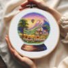 57 Cross stitch embroidery of a summer glass ball scene with a house and sunflowers, displayed in a wooden hoop