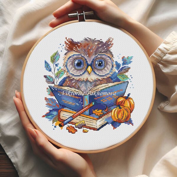 57 Autumn bookworm owl cross stitch pattern in a wooden hoop with pumpkins, books, and warm seasonal colors.
