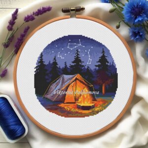 Embroidery hoop with winter camping cross stitch pattern featuring snowy mountain landscape, tent and night sky