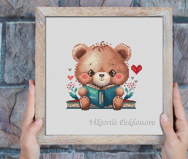 Framed cross stitch of a woodland bear reading a book with cozy floral accents