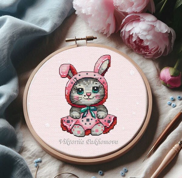 93 Cross stitch embroidery of a baby cat in a bunny costume displayed in a wooden hoop.