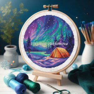 Embroidery hoop with aurora borealis camping cross stitch pattern featuring Northern Lights, tent and snowy mountain landscape