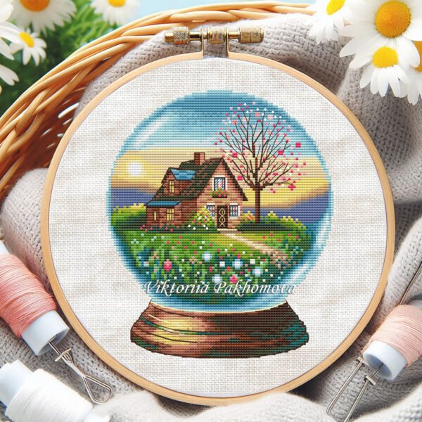 Cross stitch embroidery of a spring glass ball scene with a garden house and colorful flowers in a wooden hoop