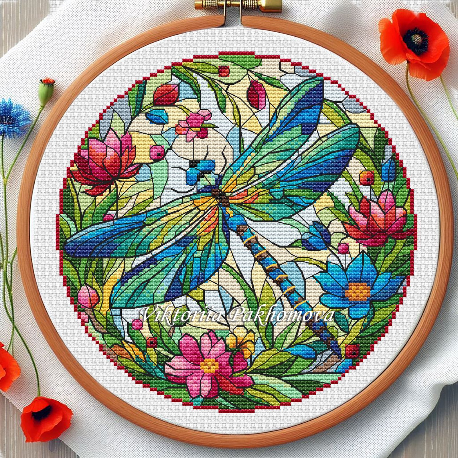 Stained glass dragonfly cross stitch pattern with vibrant blue and green wings, floral mosaic background and wooden embroidery hoop