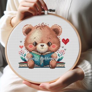 screen Cross stitch embroidery of a cute bookish bear reading a book with small hearts and floral details in a wooden hoop