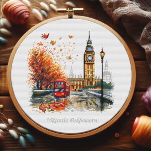 London autumn cityscape cross stitch pattern in an embroidery hoop, featuring Big Ben, a red bus, and falling leaves.