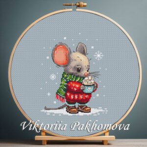 Winter baby mouse cross stitch in a wooden hoop wearing a red sweater and green scarf holding a cup with snowflakes