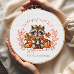 Autumn coffee raccoon cross stitch pattern with cute raccoon holding coffee cup, pumpkins, and fall leaves surrounded by “Happy Vibes” text in embroidery hoop