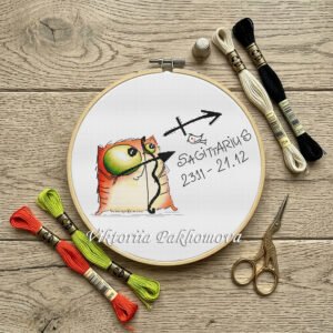 Sagittarius cross stitch pattern displayed in a hoop featuring a cute orange cat archer and zodiac arrow symbol.